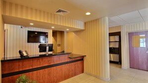 A reception area with a wooden reception desk, a flat-screen TV, a telephone, and a coffee machine. - Cobblestone Inn & Suites - Brillion (Brillion)