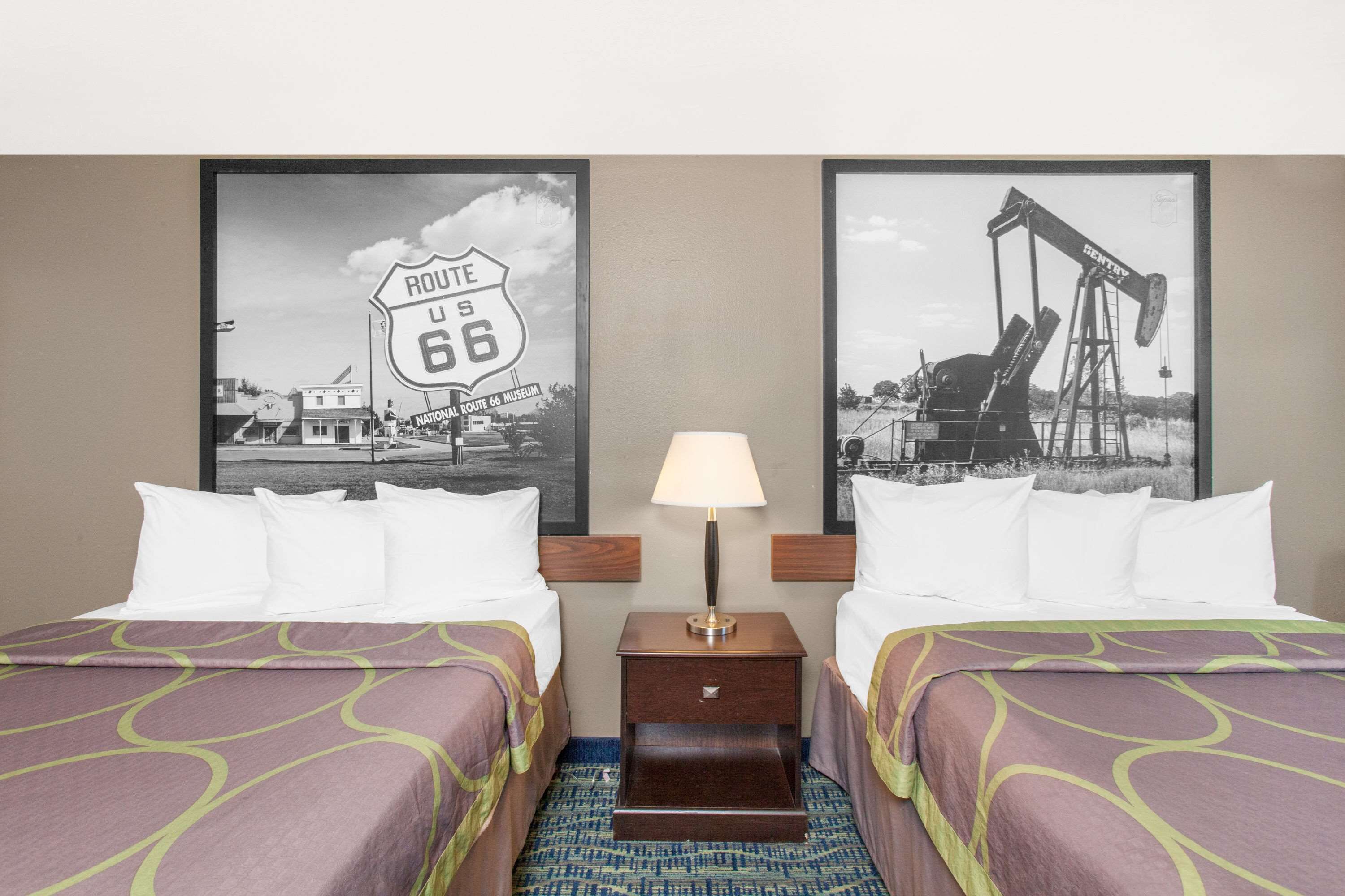 A hotel room with two beds, a nightstand with a lamp, and two framed pictures on the wall.