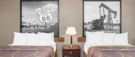 A hotel room with two beds, a nightstand with a lamp, and two framed pictures on the wall.