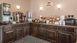 Un coin cuisine équipé d’une machine à café, d’un four à micro-ondes et d’un espace dédié au café, avec des tasses et un panier de fruits.