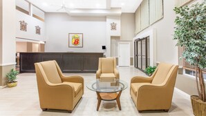 Un hall d’entrée spacieux avec un comptoir de réception, deux fauteuils beiges, une table basse en verre et une grande plante en pot.