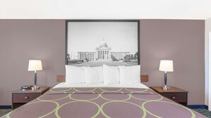 Une chambre d’hôtel avec un grand lit, deux tables de chevet avec des lampes, un tableau encadré représentant un bâtiment accroché au mur et une couvre-lit à motifs.