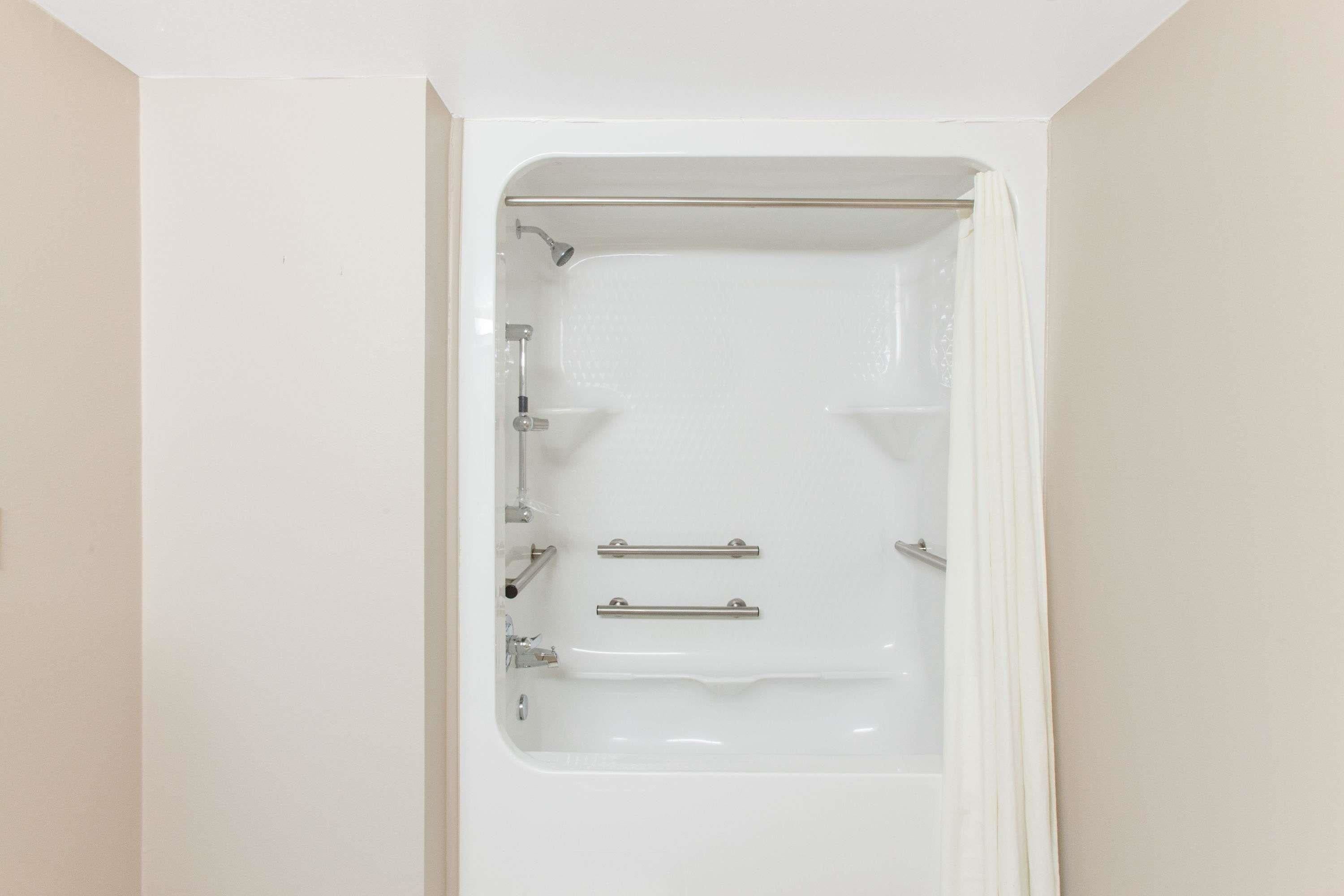 Una bañera blanca con ducha, barras de apoyo y panel de control.