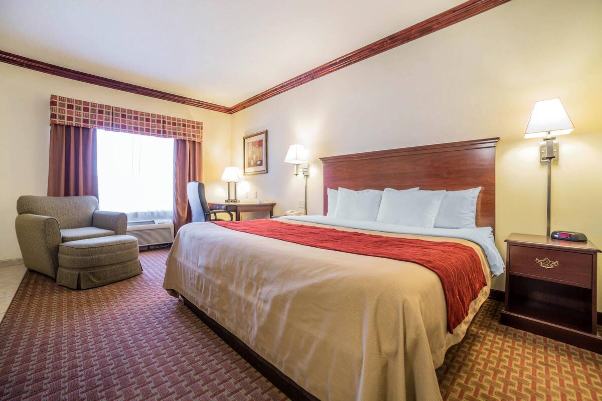 A hotel room with a large bed, a chair, a desk, and a nightstand.