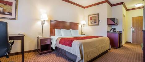 A hotel room with a bed, desk, chair, lamp, and artwork on the walls.