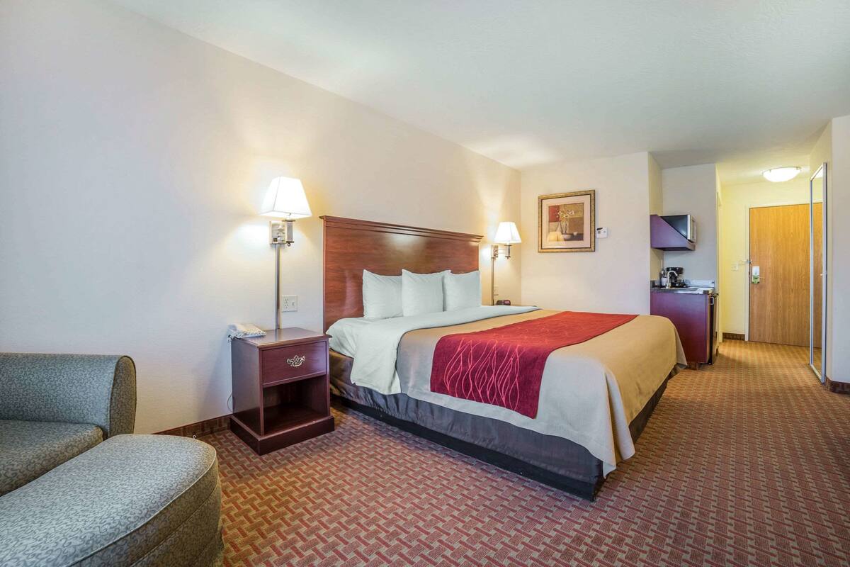 A hotel room with a bed, two bedside lamps, a desk with a telephone, a chair, and a door leading to the bathroom.