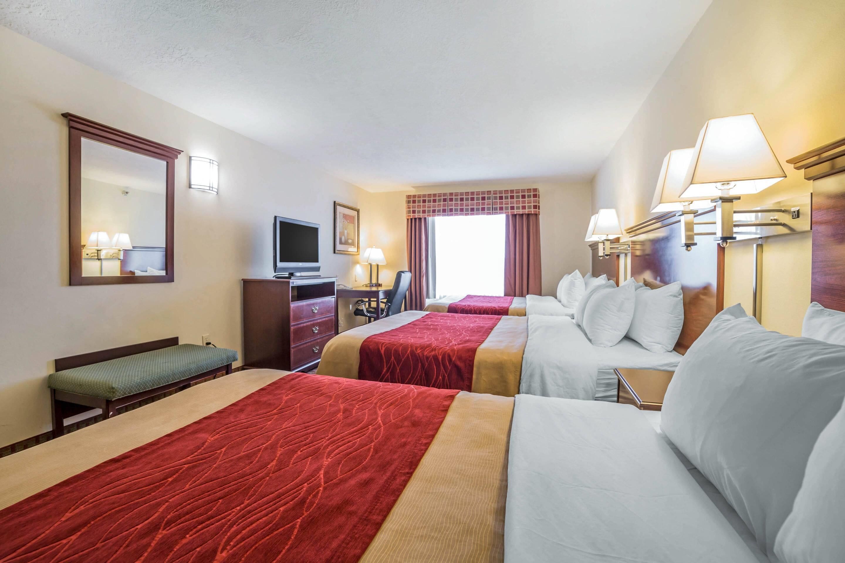 Habitación de hotel con dos camas, un escritorio, televisión y ventana con cortinas.