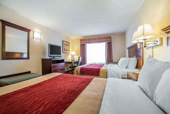 A hotel room with two beds, a desk, a television, and a window with curtains.