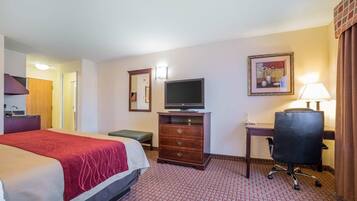 Een hotelkamer met een bed, een bureau met een computer, een stoel, een televisie, een kast en een lamp.