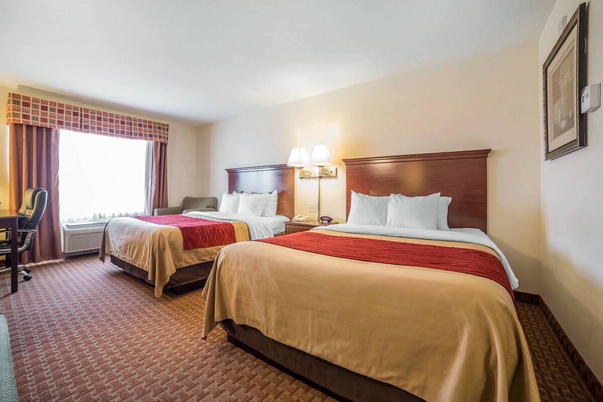 A hotel room with two beds, a desk, and a chair.