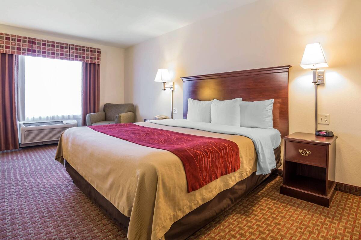 A hotel room with a large bed, two bedside lamps, a chair, and a nightstand.