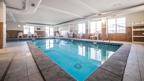 Una piscina interior con agua cristalina, rodeada de sillas blancas y suelo de baldosas.