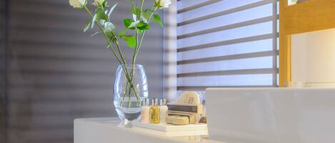 Un vase blanc contenant des roses blanches, posé sur une surface blanche, à côté d’une bouteille et d’une boîte portant l’inscription « MOTION BROWN ».