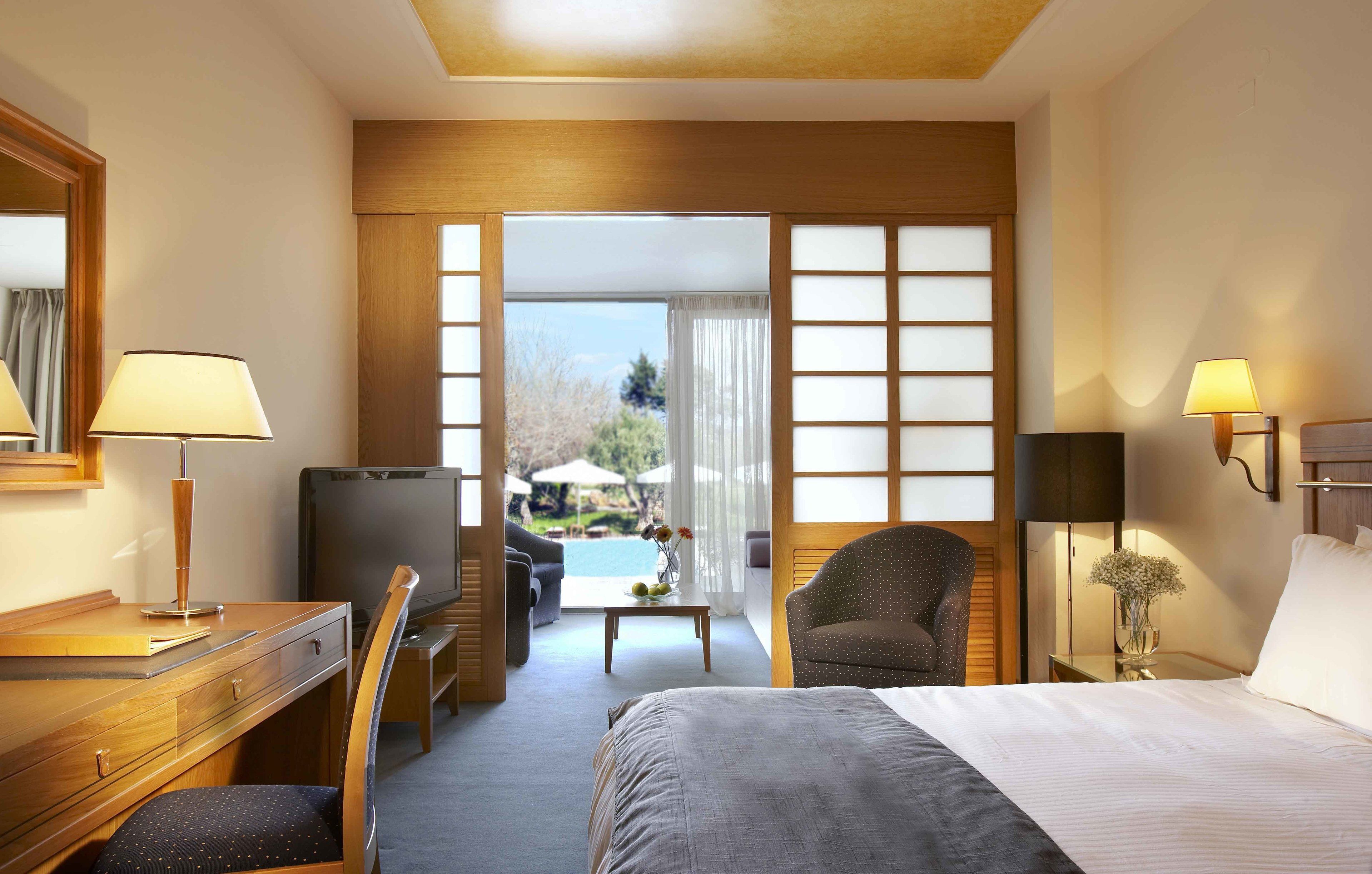 A hotel room with a bed, desk, chair, TV, and a view of an outdoor pool.