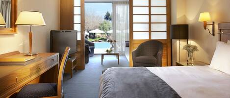 Habitación de hotel con cama, escritorio, silla, televisor y vista a una piscina al aire libre.