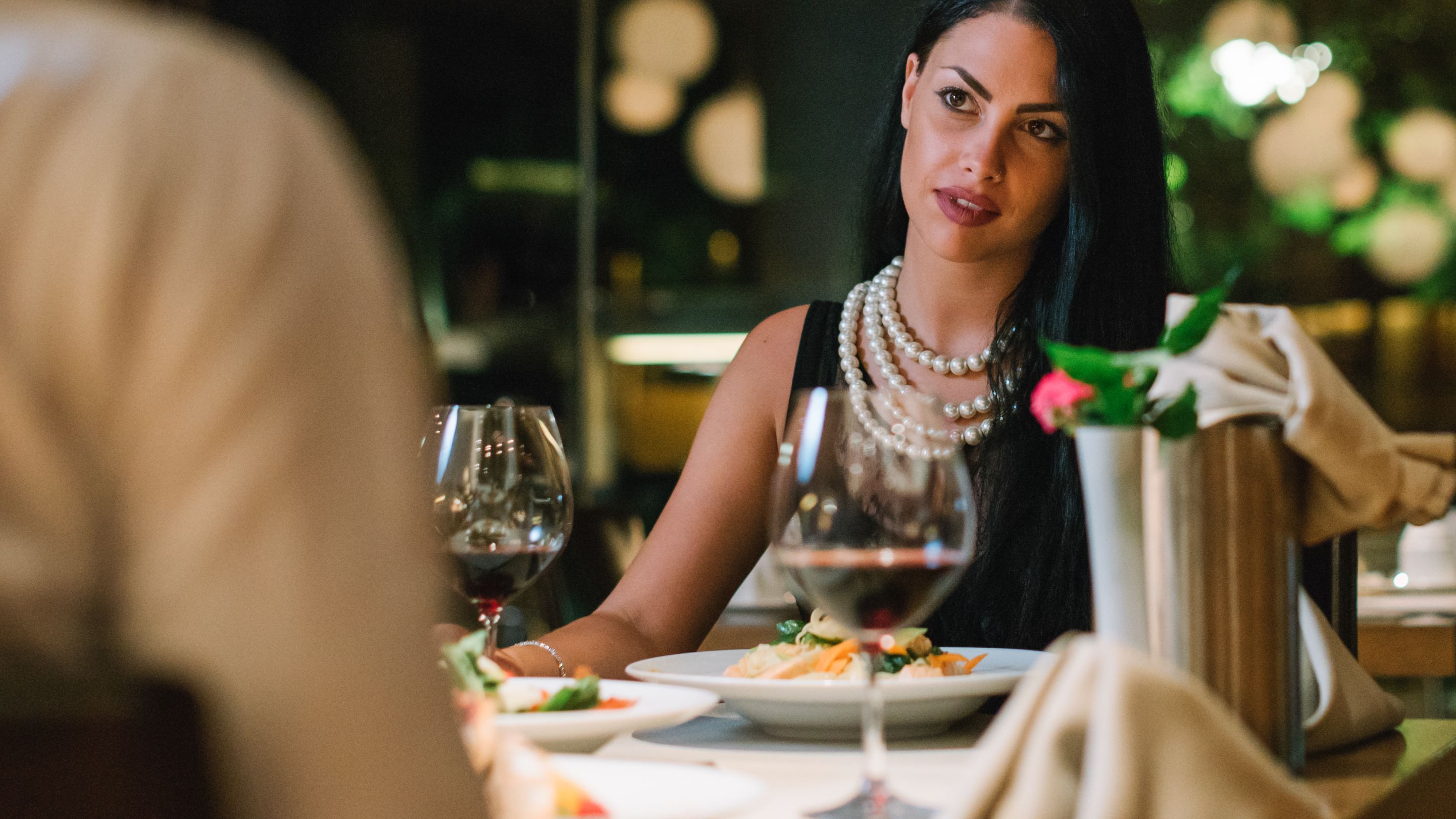 Una mesa de comedor con platos de comida, copas de vino y un jarrón con una flor.