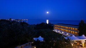 Een modern hotel met terras, uitzicht op zee, een maanverlichte nacht en een verafgelegen stadsbeeld.