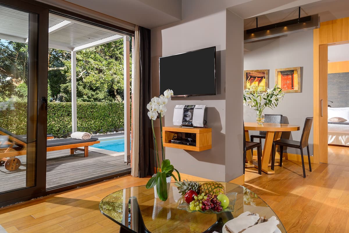 Une chambre d’hôtel moderne avec une table en verre, un téléviseur fixé au mur, un lit et un petit coin repas.
