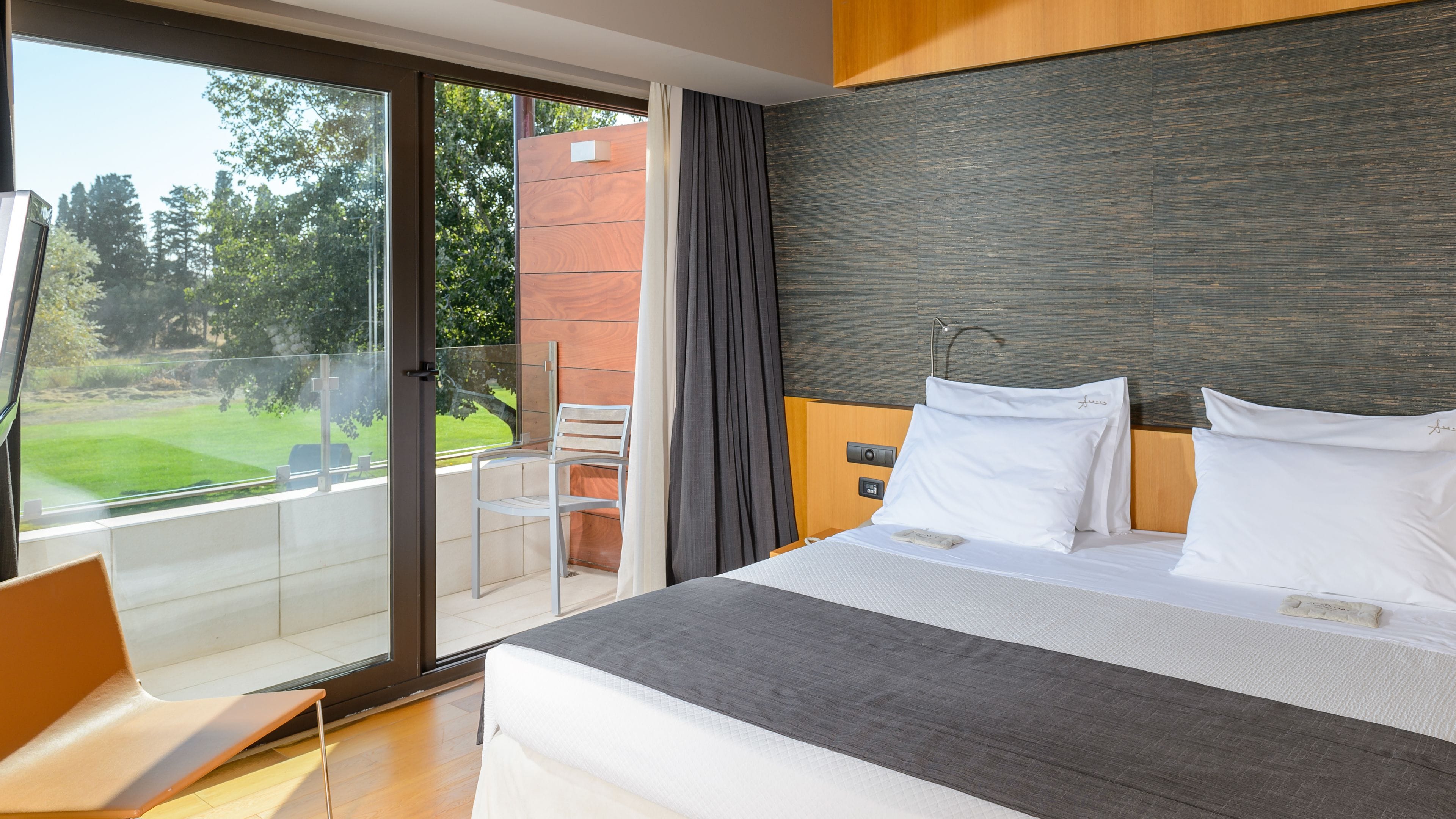 A modern hotel room with a large bed, a view of a garden, and a sliding glass door to the outdoors.