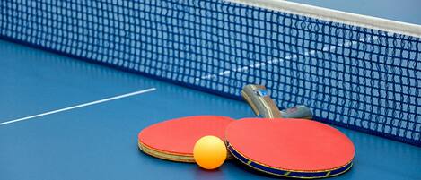 A blue table tennis table with two red paddles and a yellow ball.