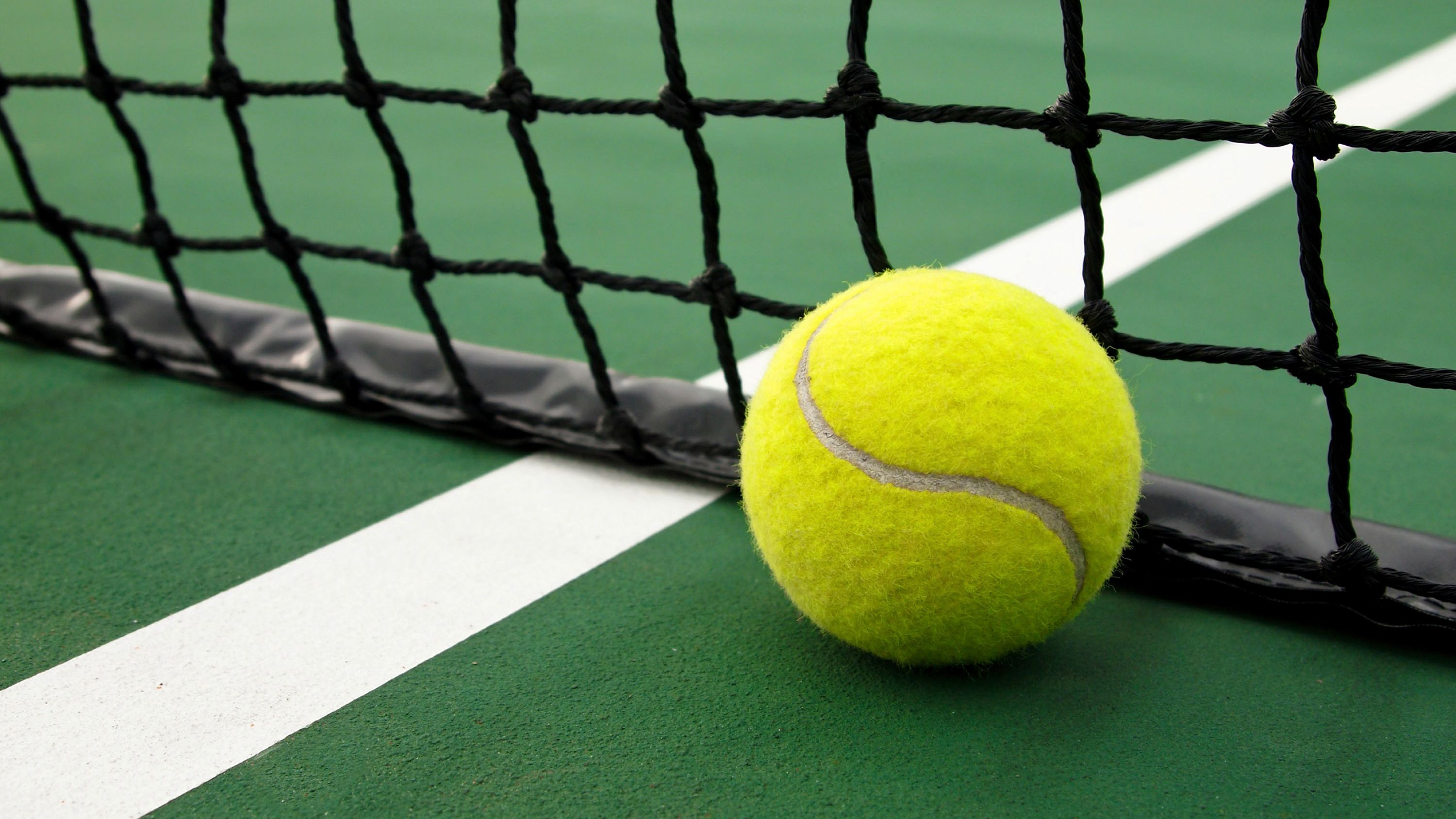 Een tennisbal op een groene baan met witte lijnen.