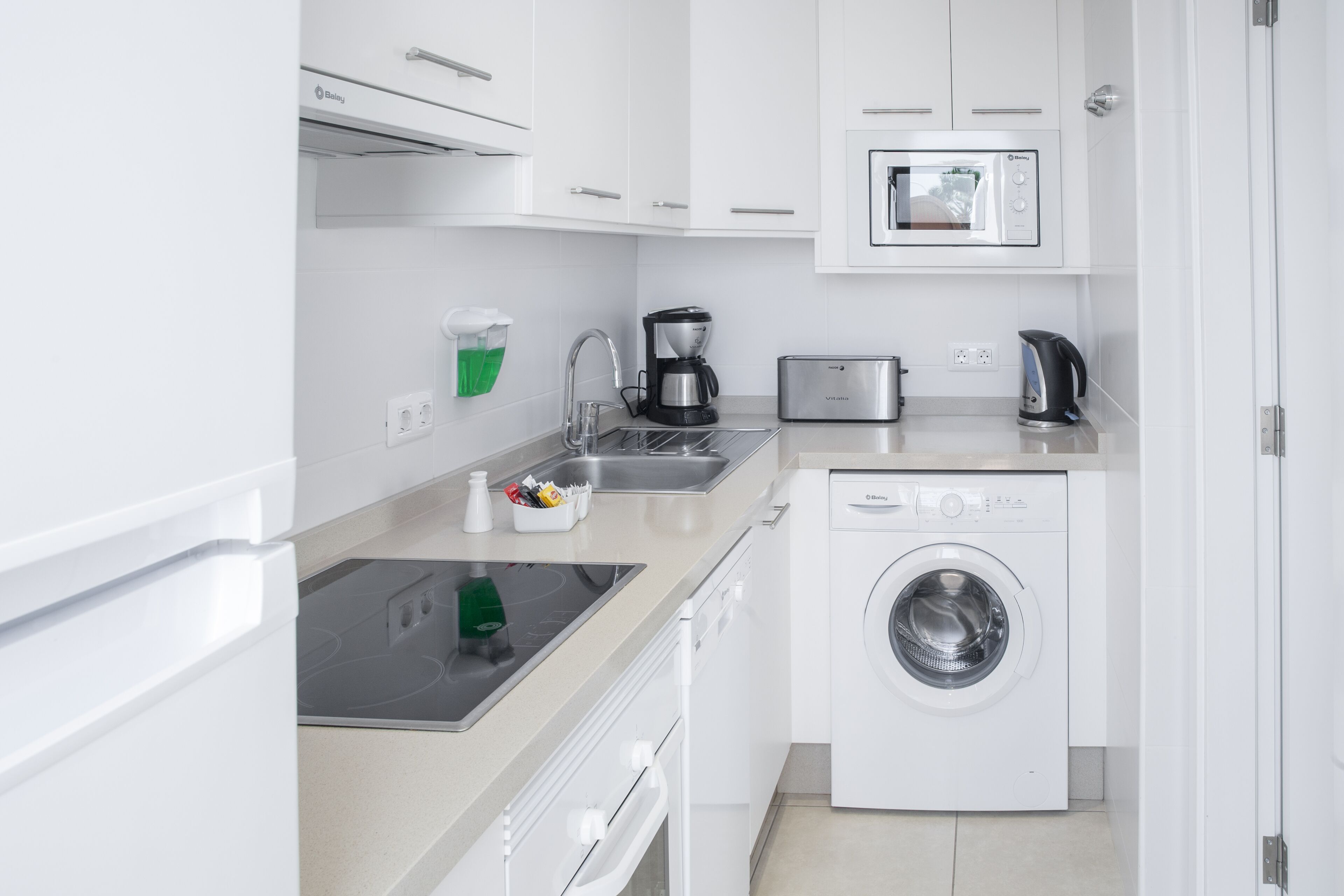 A compact kitchen with a built-in washing machine, a microwave, and a coffee maker.