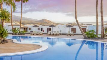 Una piscina con sillas de descanso, palmeras y vistas a las montañas.