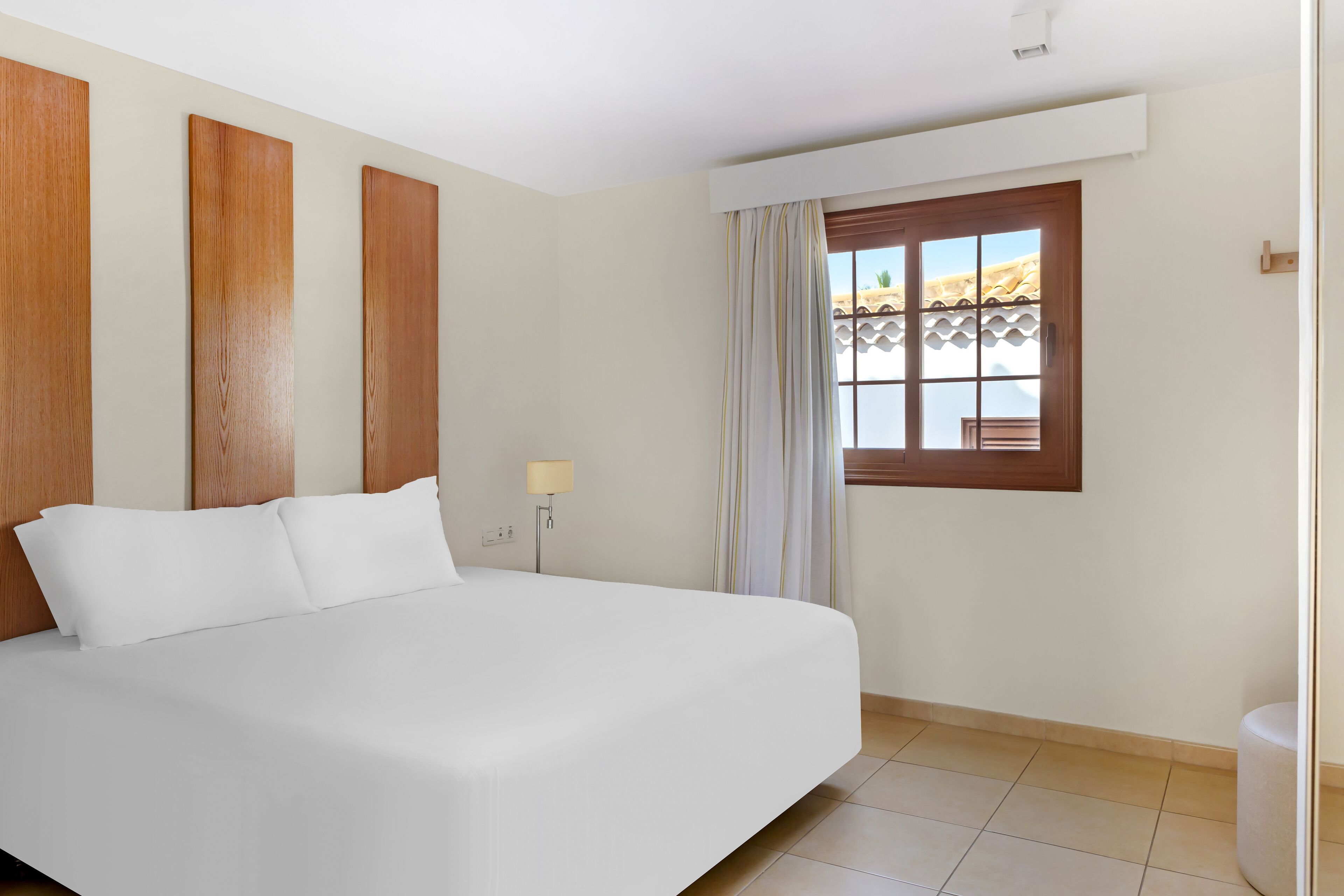 A hotel room with a large bed, a window with curtains, and a view of the outdoors.