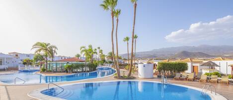 A resort pool area with multiple swimming pools, palm trees, and lounge chairs.