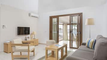 Un salon moderne comprenant un canapé, une table en bois, un téléviseur et une porte-fenêtre coulissante donnant sur un espace extérieur.