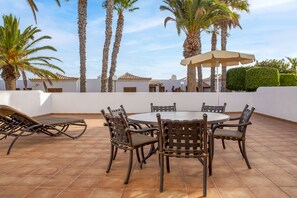Eine Terrasse mit rundem Tisch und Stühlen, umgeben von Palmen und einer weißen Mauer.