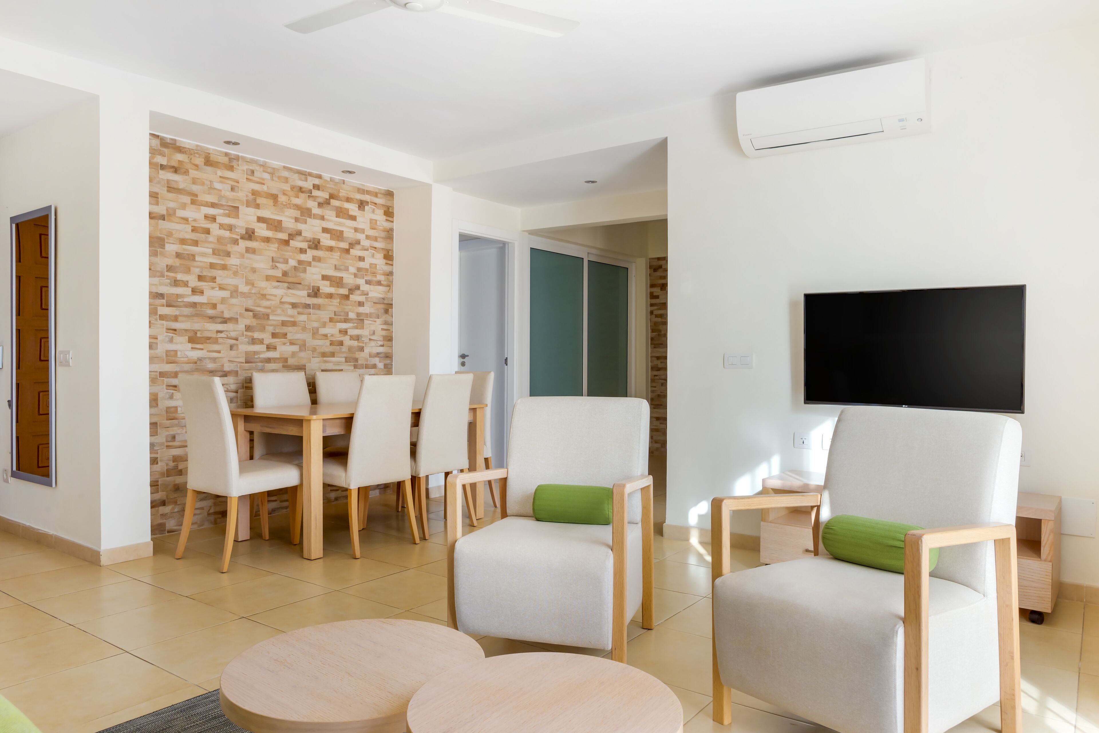 A modern living room with a dining area, a flat-screen TV, and a brick-patterned wall.