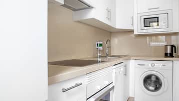 A modern kitchen with white cabinets, a stainless steel sink, a microwave, a coffee maker, and a front-loading washing machine.