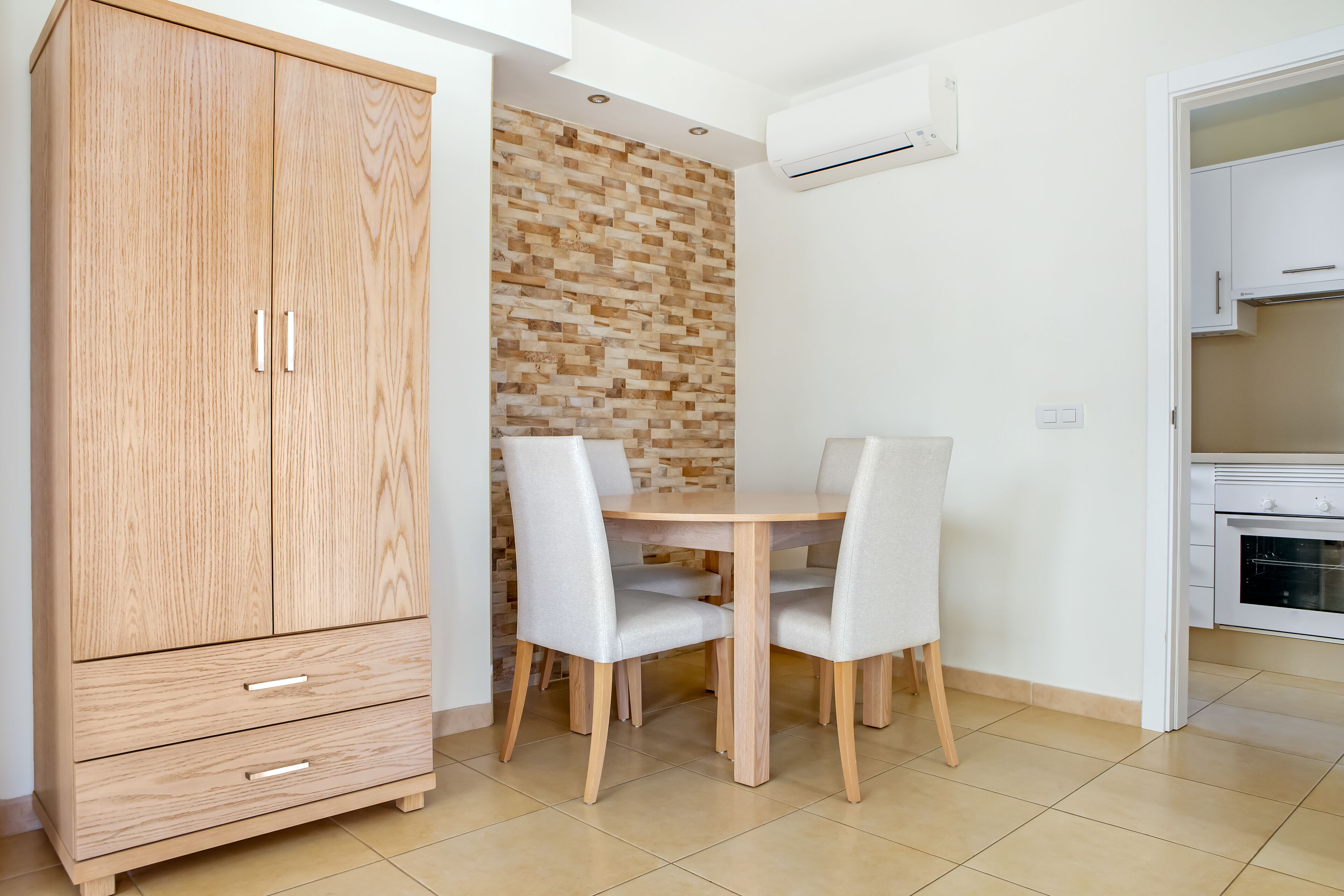 A compact kitchen with a wooden cabinet, a dining table with chairs, and a tiled floor.