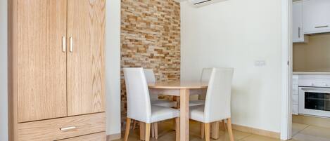 A compact kitchen with a wooden cabinet, a dining table with chairs, and a tiled floor.