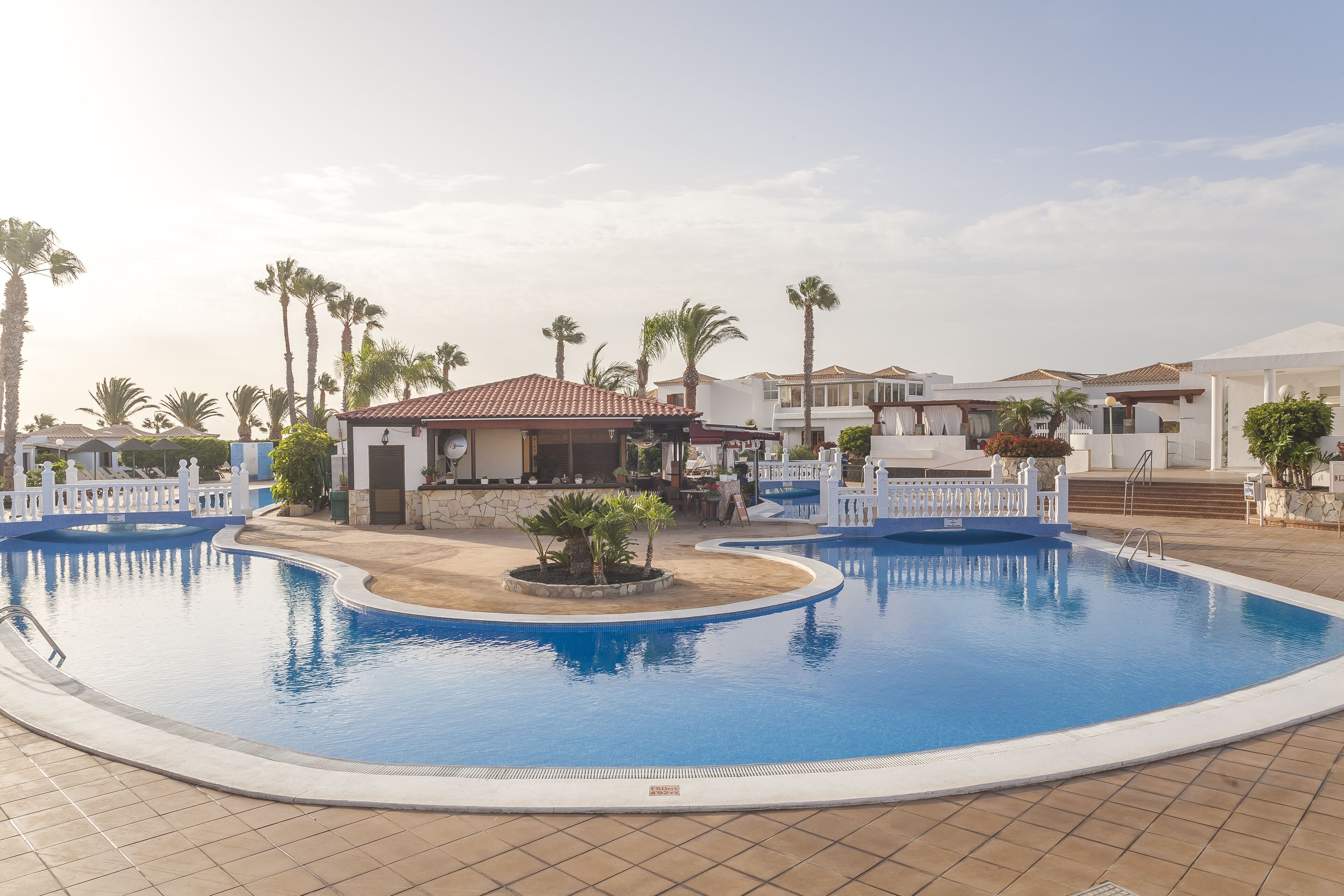 A swimming pool surrounded by palm trees and buildings with a tiled floor.
