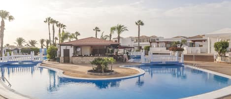 A swimming pool surrounded by palm trees and buildings with a tiled floor.