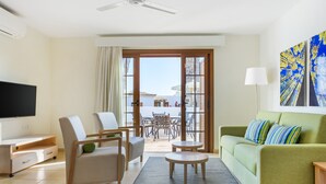 Uma sala de estar moderna com televisão de tela plana, um sofá verde, duas poltronas, uma mesa de centro e uma varanda com vista.