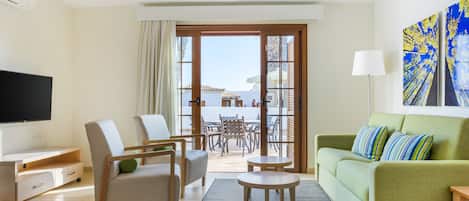 A modern living room with a flat-screen TV, a green sofa, two armchairs, a coffee table, and a balcony with a view.