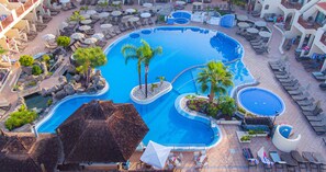 A large outdoor swimming pool surrounded by lounge chairs and umbrellas, with palm trees and a small waterfall feature. - Hilton Vacation Club Royal Sunset Beach Club Tenerife (Adeje)