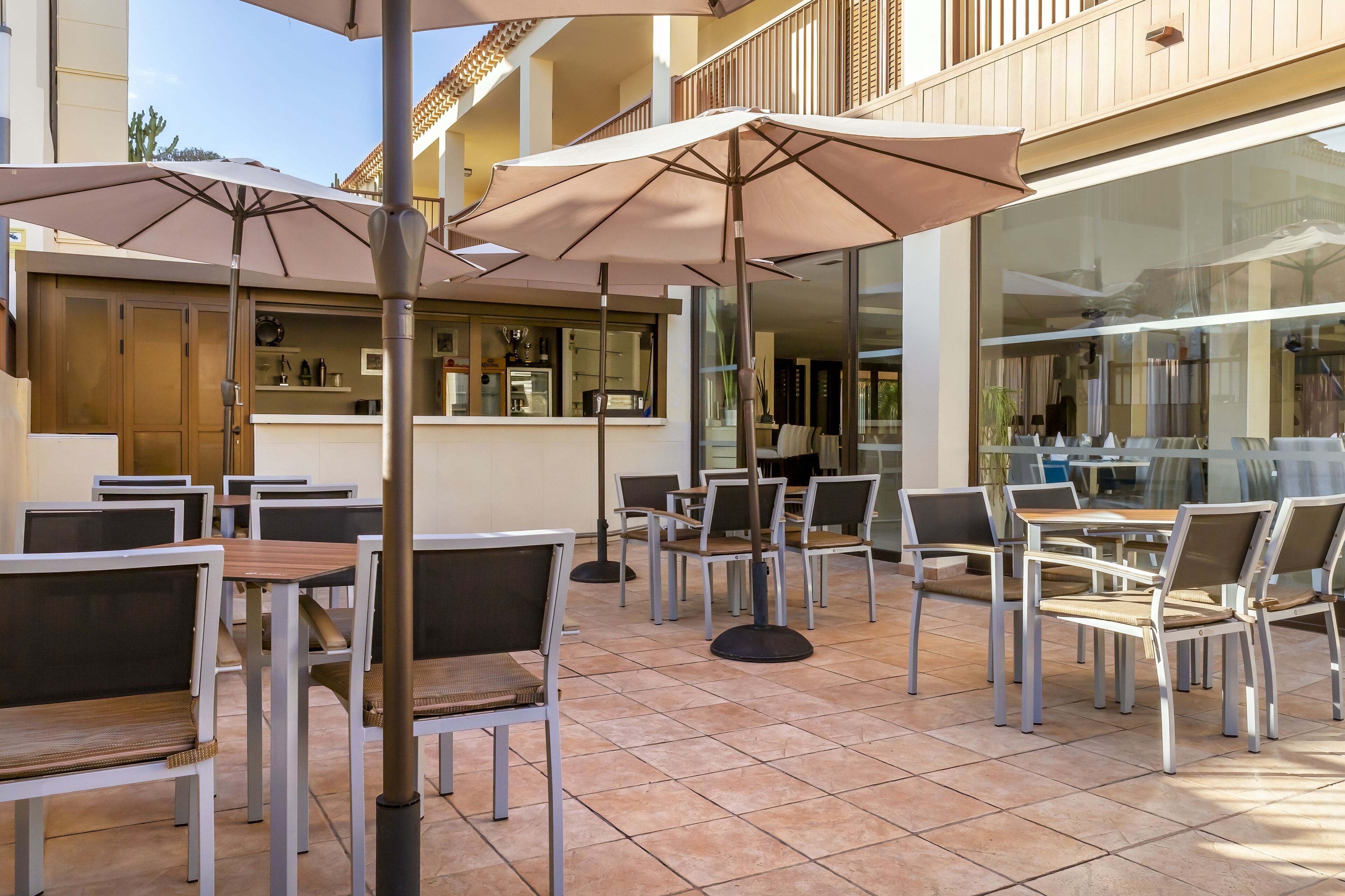 An outdoor patio area with tables and chairs, umbrellas, and a bar area.