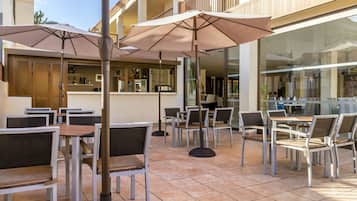 An outdoor patio area with tables and chairs, umbrellas, and a bar area.