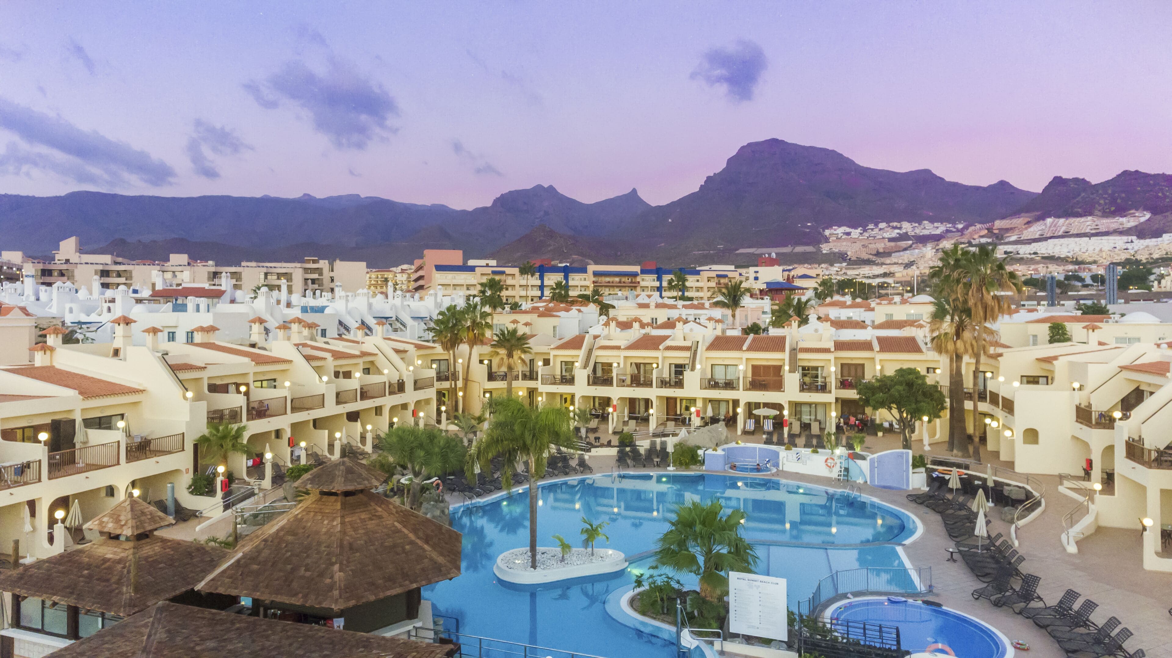 A resort with multiple swimming pools, a beach club, and a mountainous backdrop.