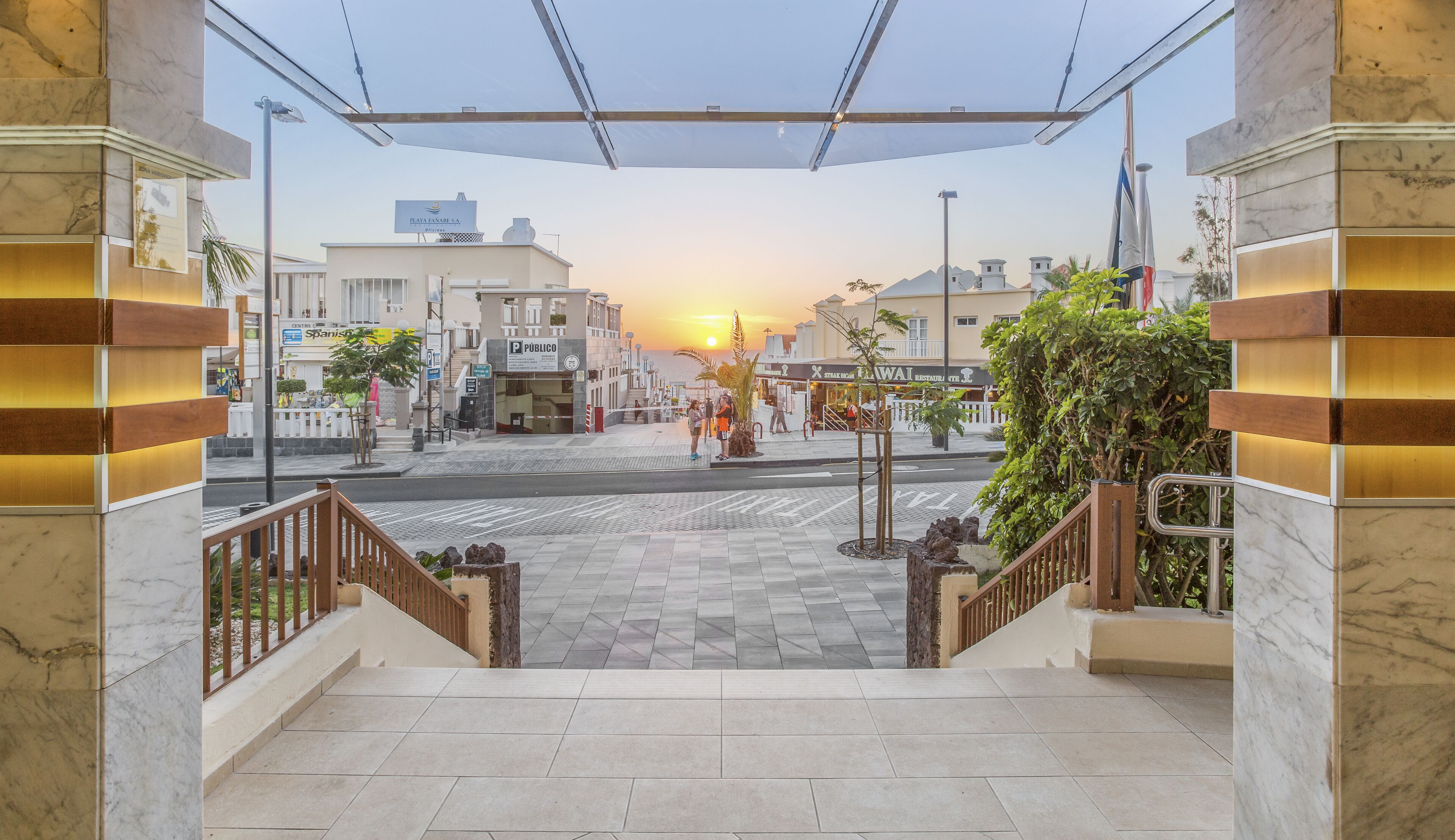 A hotel entrance with a view of the sunset, a public parking sign, and a restaurant named "STAKEHOUSE".