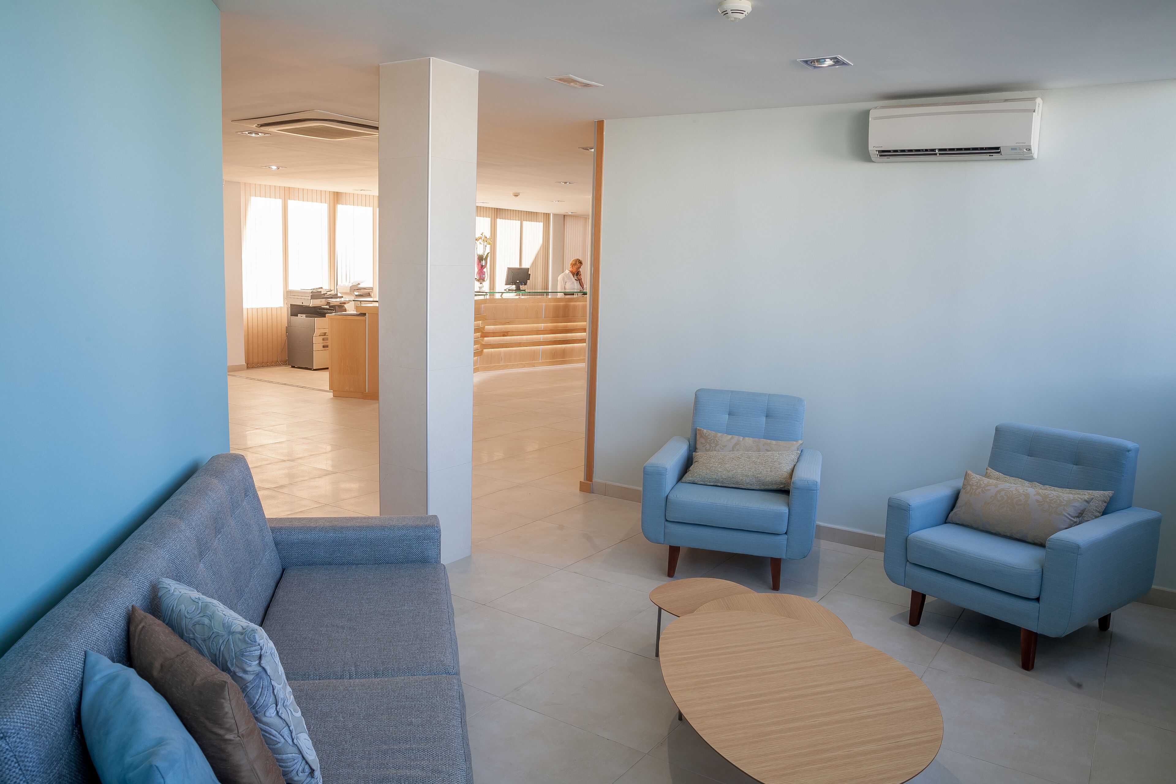 Una sala de estar moderna con un sofá, dos sillones y una mesa de centro. Una escalera conduce a un comedor al fondo.