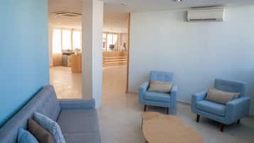 Una sala de estar moderna con un sofá, dos sillones y una mesa de centro. Una escalera conduce a un comedor al fondo.