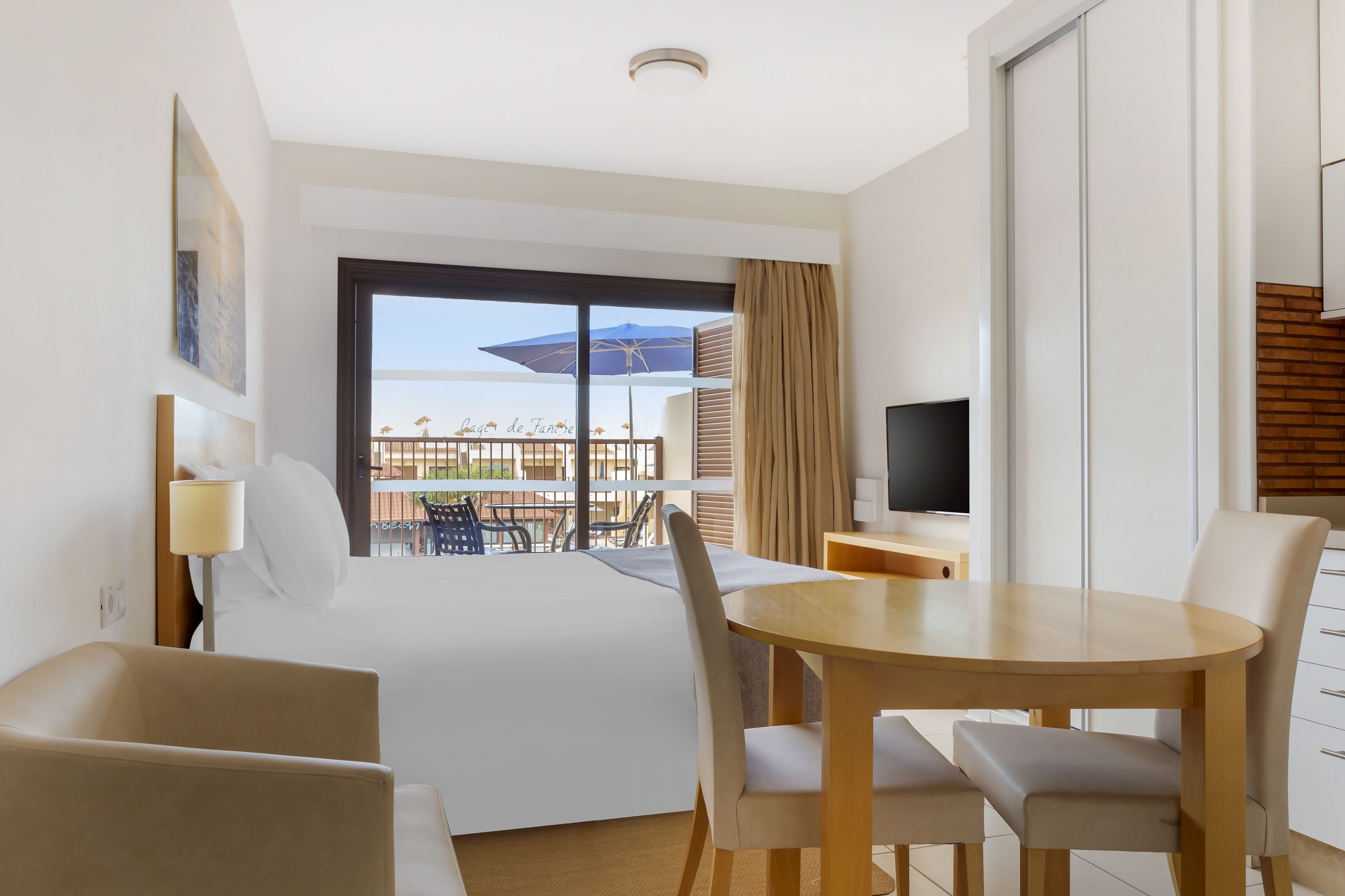 Ein Hotelzimmer mit Bett, Fernseher, Esstisch mit Stühlen und einem Balkon mit Aussicht.