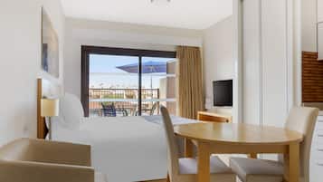 A hotel room with a bed, a TV, a dining table with chairs, and a balcony with a view.