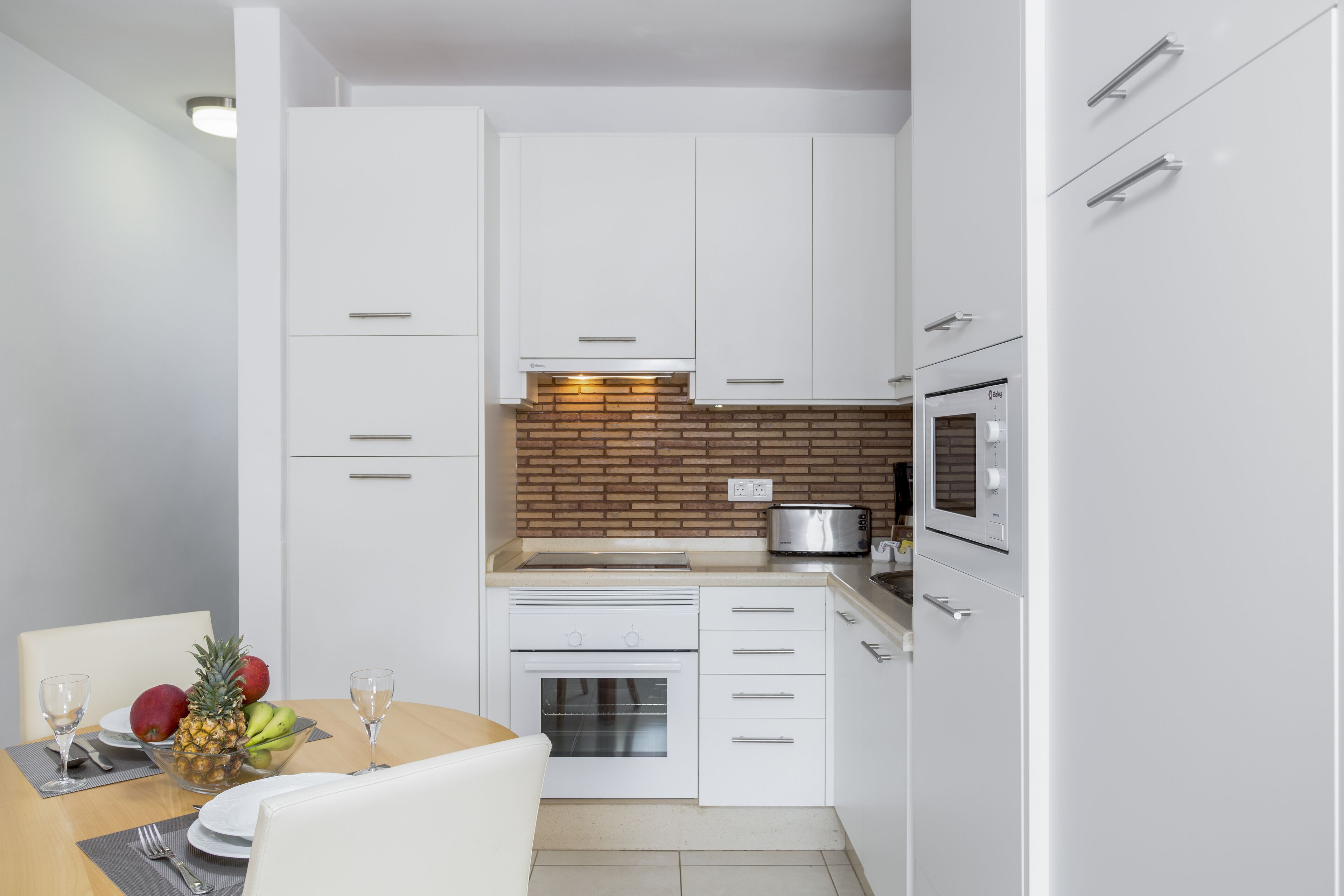 A compact kitchen with white cabinetry, a brick backsplash, and a built-in oven.