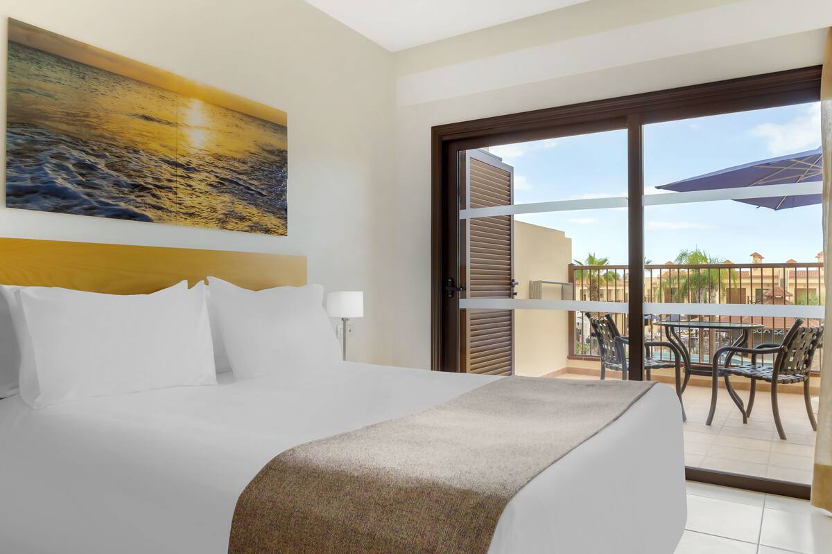 Quarto de hotel com cama, pintura, varanda com mobiliário exterior e vista para o exterior.